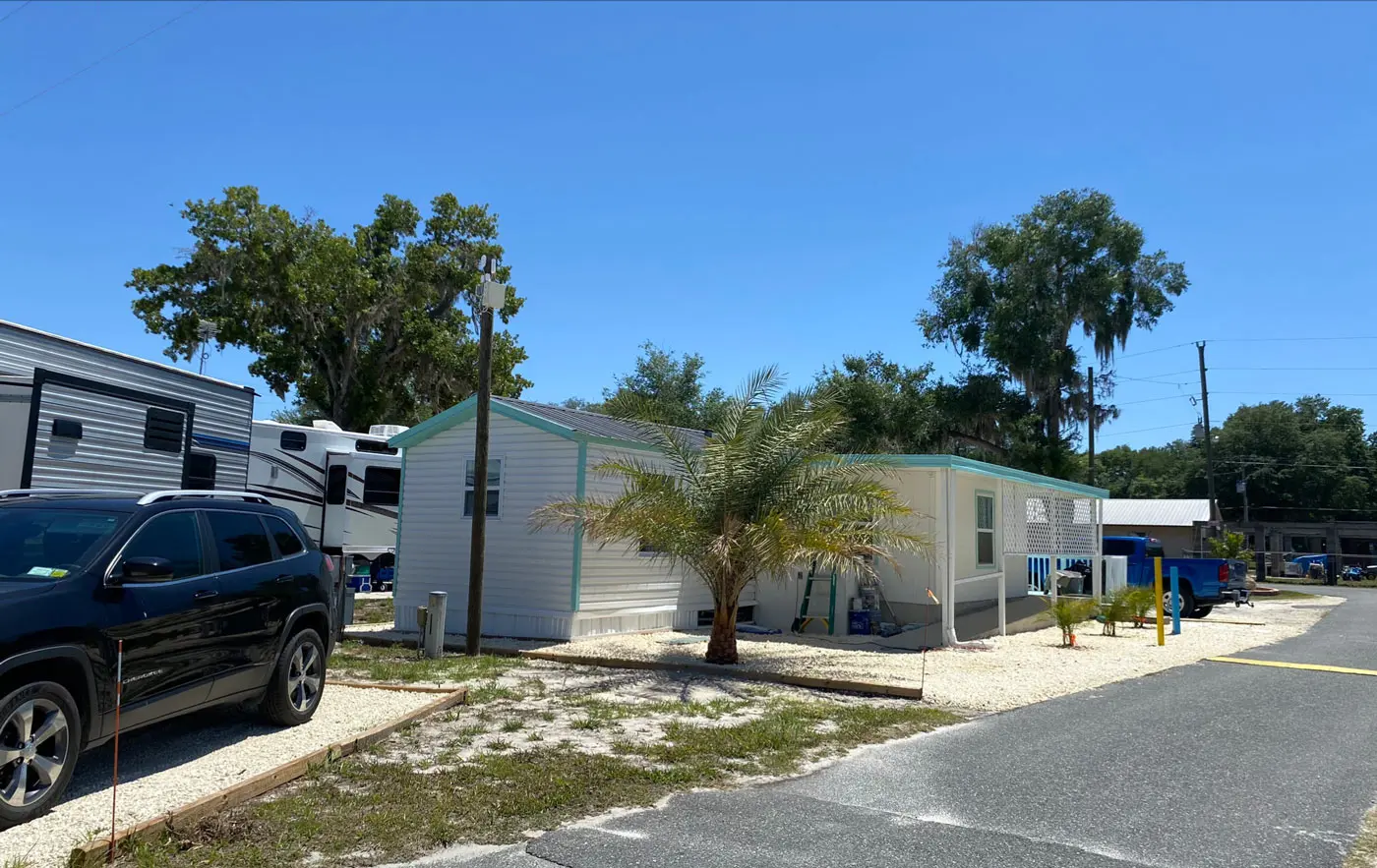 Mobile home with palm trees and Spanish-moss oaks under blue Florida sky